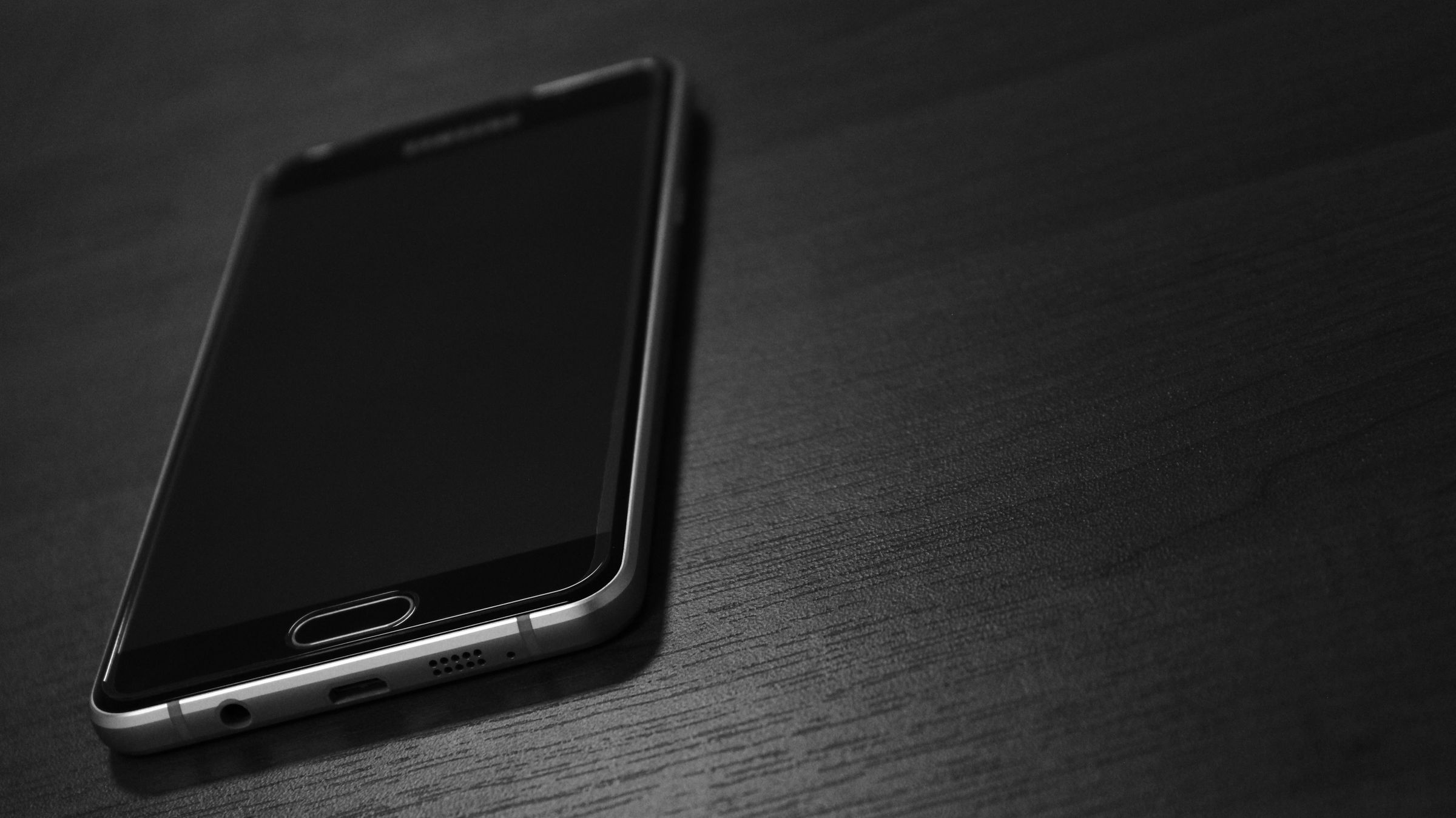 Smartphone di atas meja gelap, service HP & iPhone Malang & Semarang di Servisin Kuy